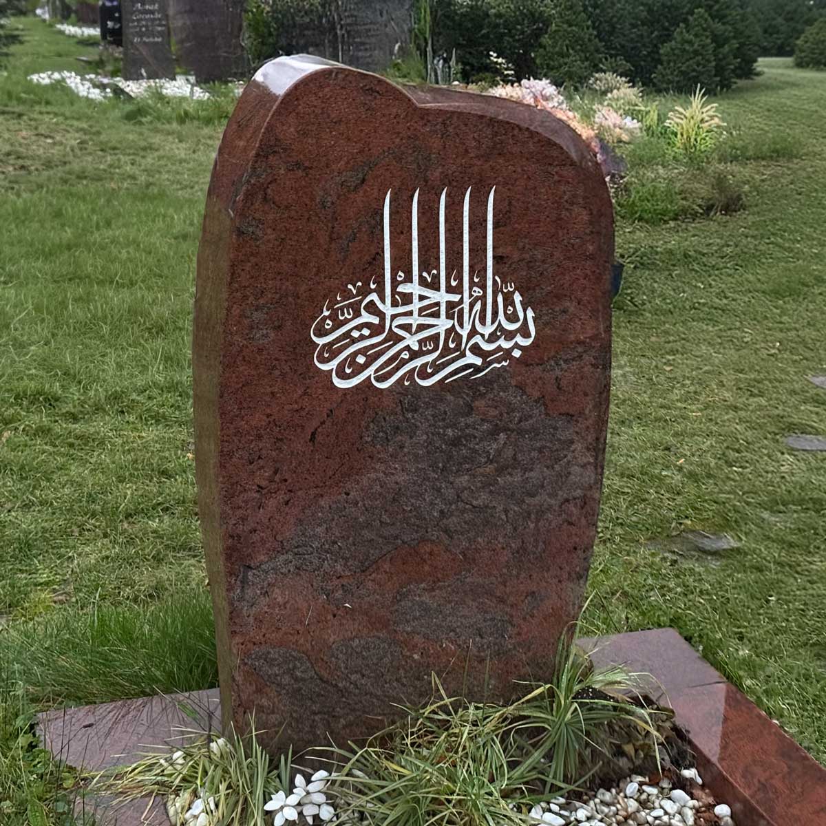 Muslimischer Grabstein Rukbah: rötliche organisch geformte Stele mit weißer Basmala-Kalligrafie Hauptbild